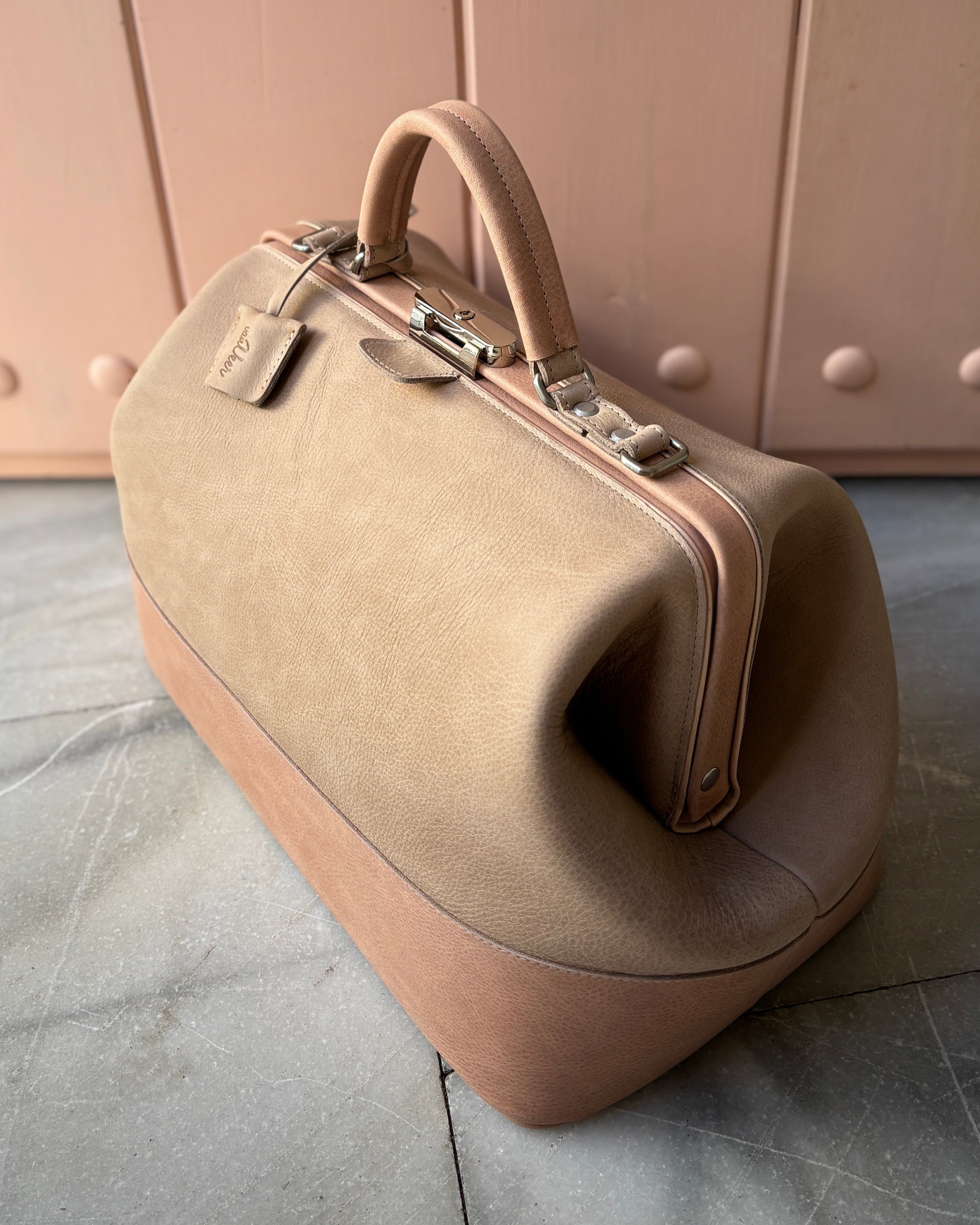 Beige doctors bag on a light gray surface with a blush pink wall in the background